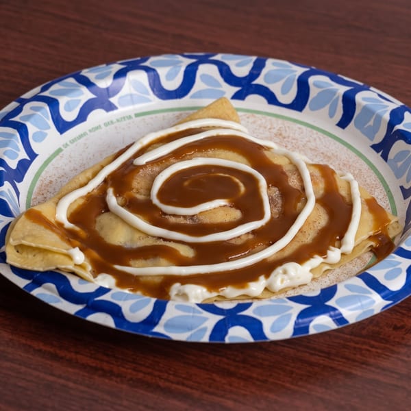 A folded crepe drizzled with caramel and white icing, served on a blue and white paper plate.