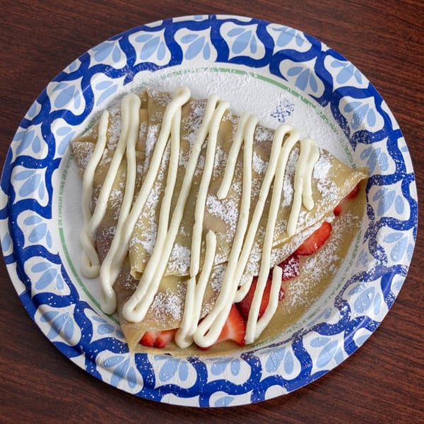 Strawberry crepe drizzled with white icing and powdered sugar on a blue and white paper plate.