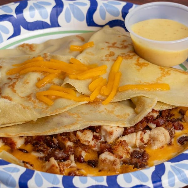 Savory crepe filled with chicken, bacon, and melted cheese, topped with shredded cheddar and a side of sauce.