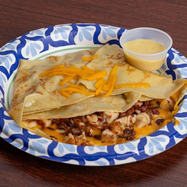 Savory crepe filled with chicken, bacon, and melted cheese, served with a side of sauce.