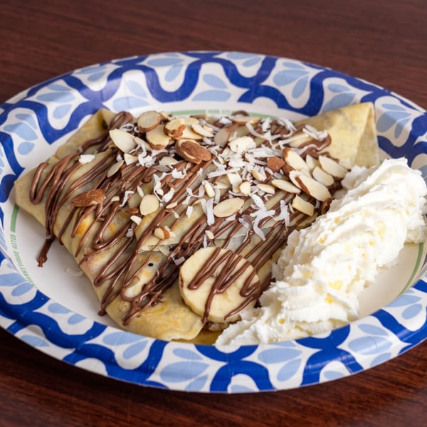 Crepe drizzled with chocolate, topped with almonds, coconut flakes, banana slices, and whipped cream.