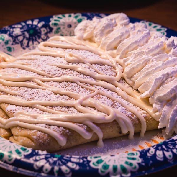 Sweet crepe drizzled with white icing, powdered sugar, and a generous dollop of whipped cream.