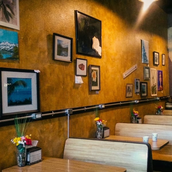 A man stands in a restaurant with mustard-yellow walls adorned with various framed pictures and art.