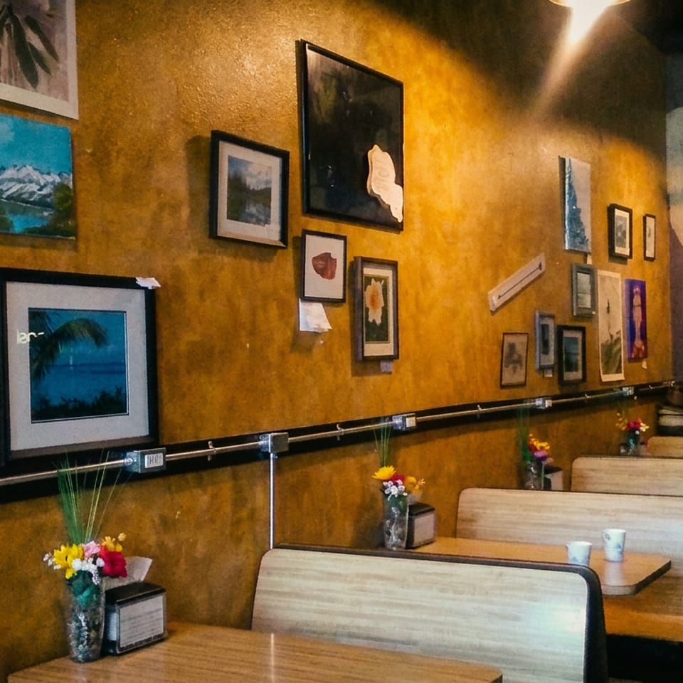 A man stands in a restaurant with mustard-yellow walls adorned with various framed pictures and art.